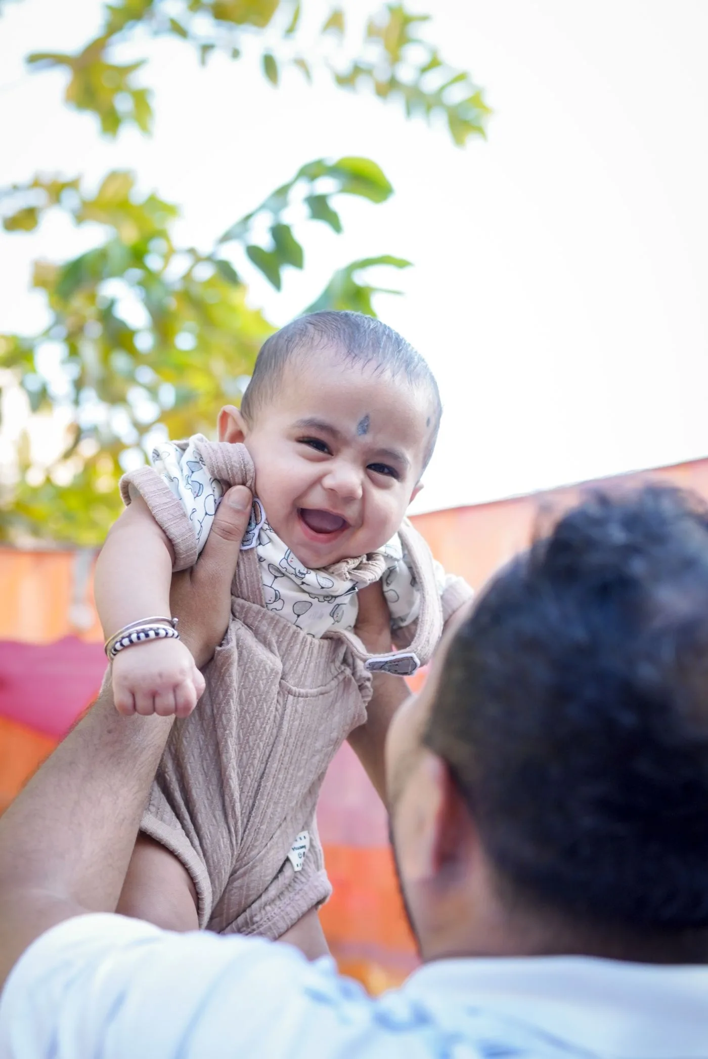 Ein Erwachsener hebt ein lächelndes Baby im Freien hoch